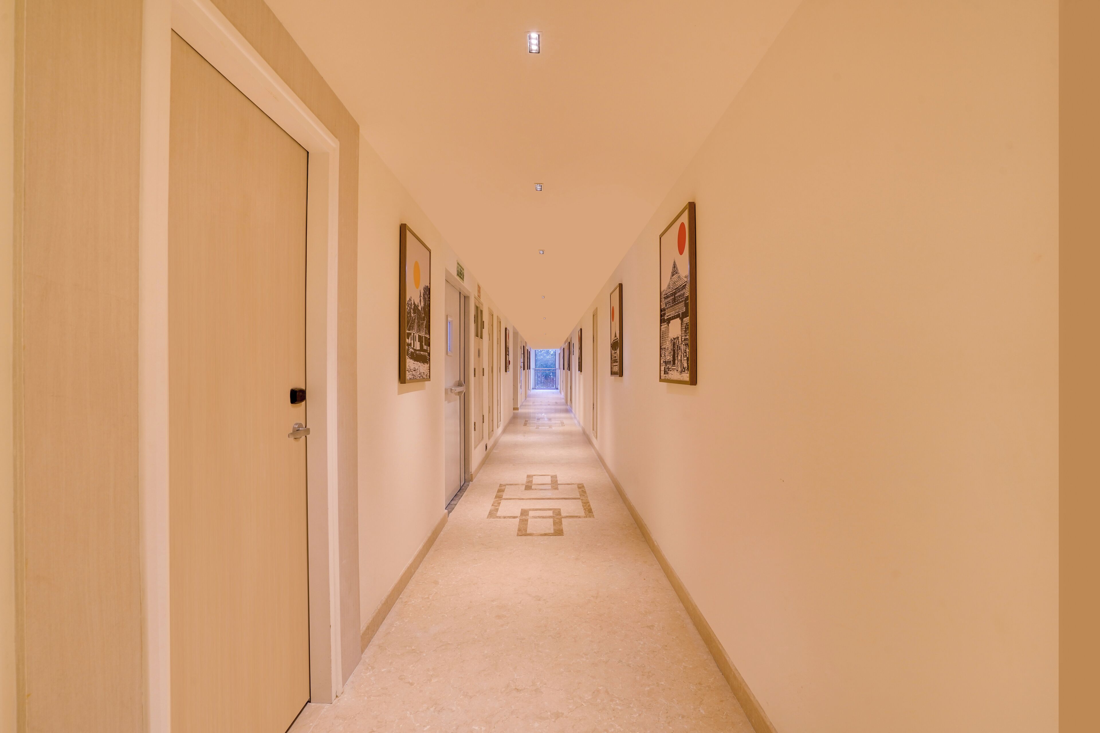 Un couloir d’hôtel avec des portes des deux côtés, des tableaux encadrés accrochés aux murs et un sol recouvert de moquette.