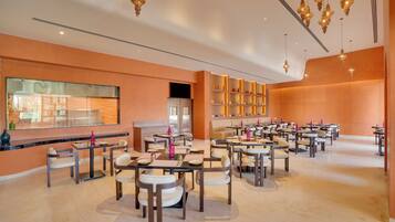 A spacious restaurant with multiple tables and chairs, a large window overlooking the street, and decorative hanging lights.