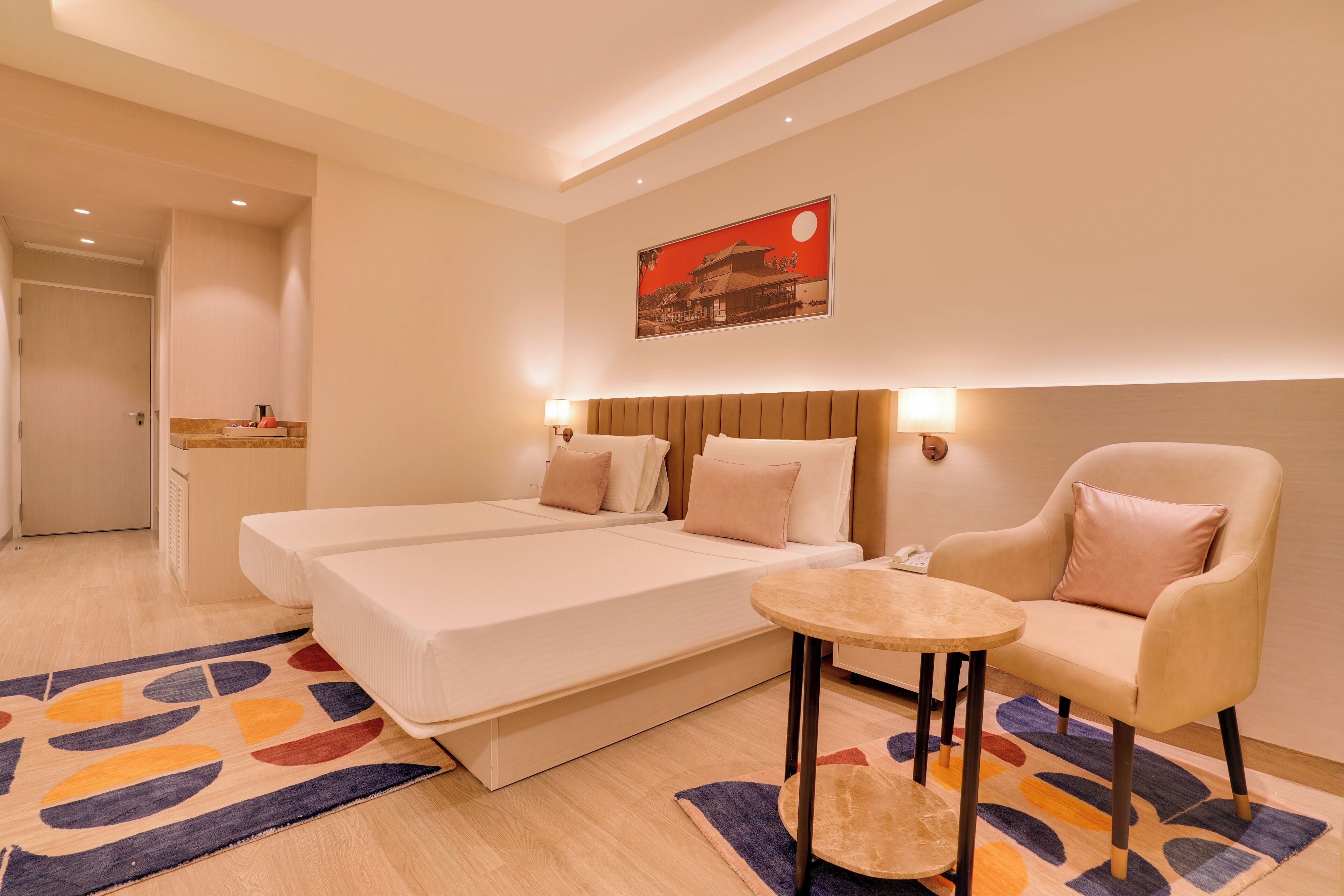 Een hotelkamer met twee bedden, een tafeltje, een stoel en een schilderij aan de muur.