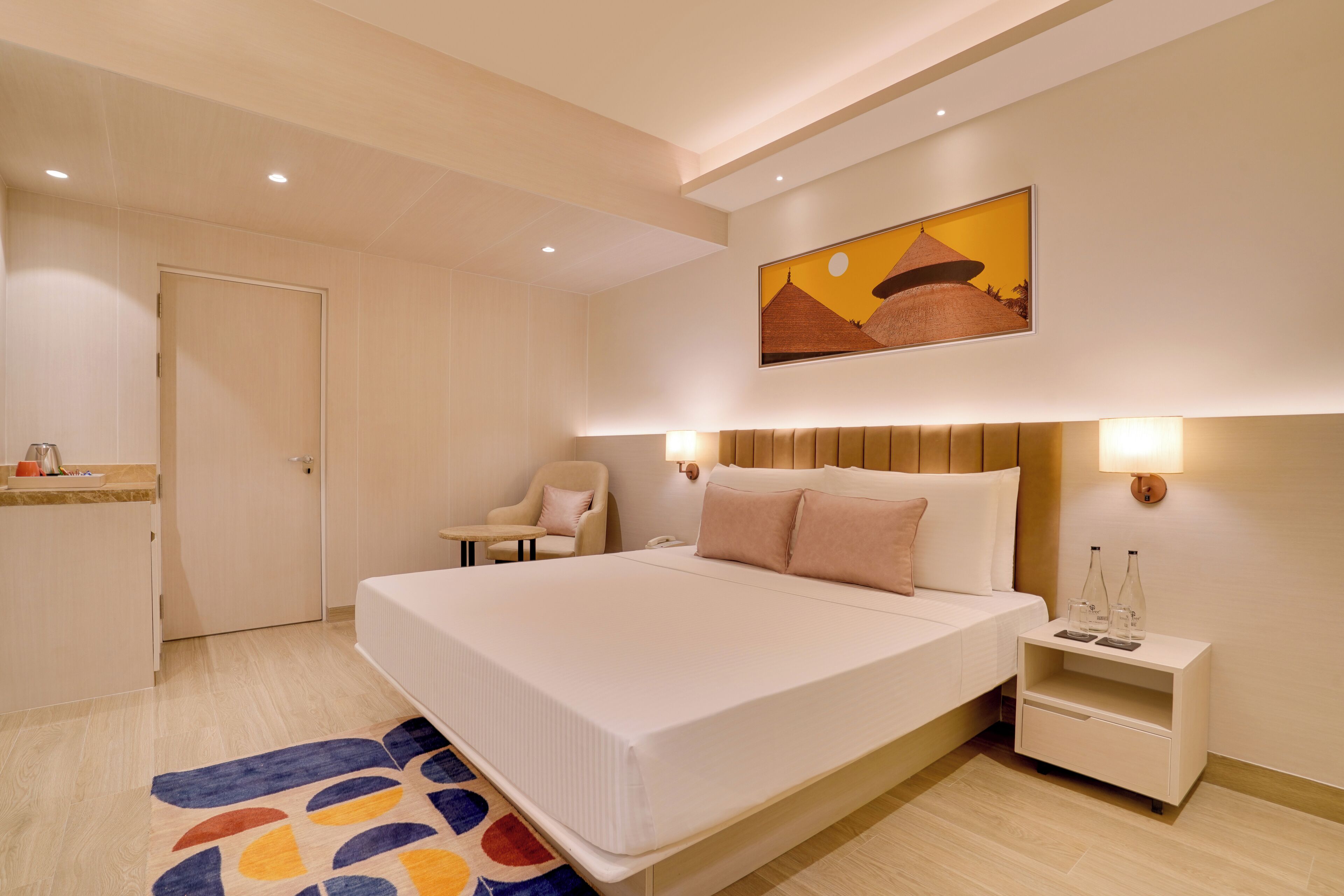 A modern hotel room with a large bed, bedside tables, a chair, and a painting on the wall.