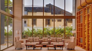 A spacious living area with a sofa set, coffee tables, and a large window offering a view of the outside. - Lemon Tree Premier Thiruvananthapuram (Thiruvananthapuram)