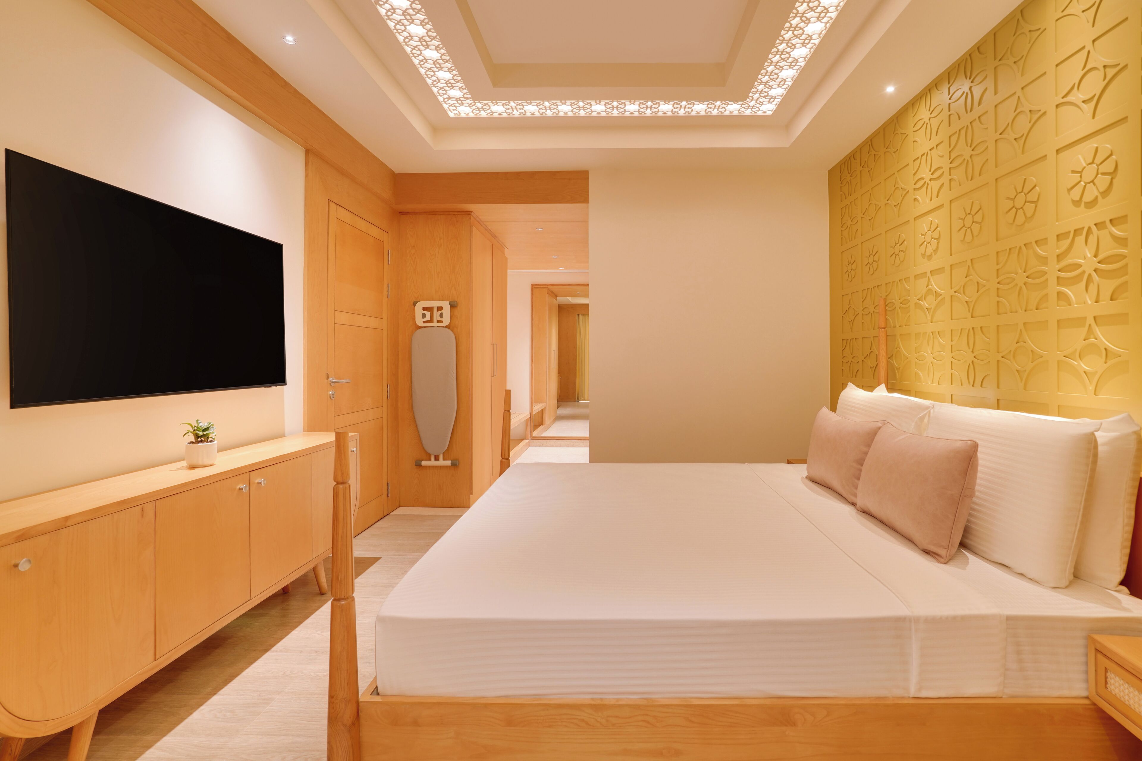 Une chambre moderne avec un grand lit, un téléviseur à écran plat, des meubles en bois et un panneau décoratif mural.