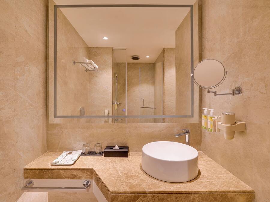 A modern bathroom with a large mirror, a round sink, and a shower area.
