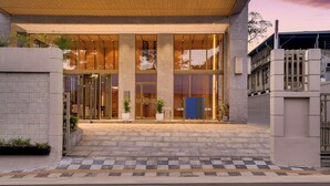 A hotel entrance with a tiled pathway leading to a glass door, columns, and potted plants. - Lemon Tree Premier Thiruvananthapuram (Thiruvananthapuram)