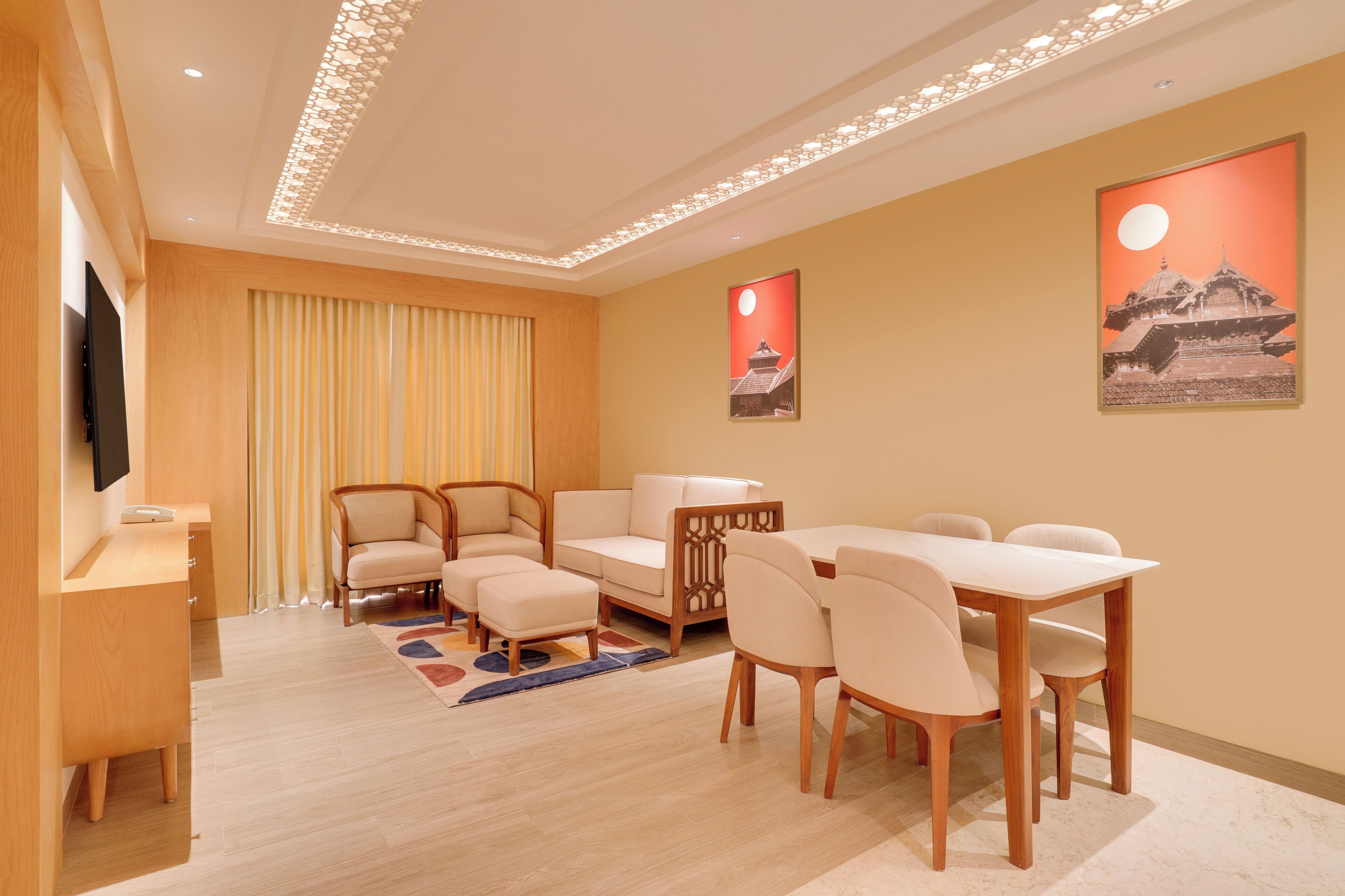 A modern hotel room with a wooden desk, a sofa, a dining table with chairs, and a TV.