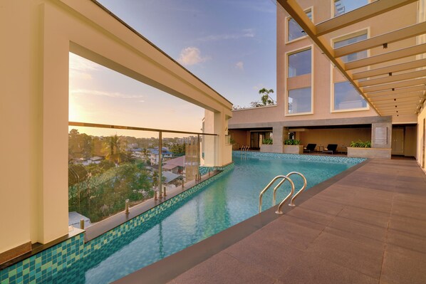 A rooftop swimming pool with clear blue water, surrounded by a modern building with large windows and a balcony.
