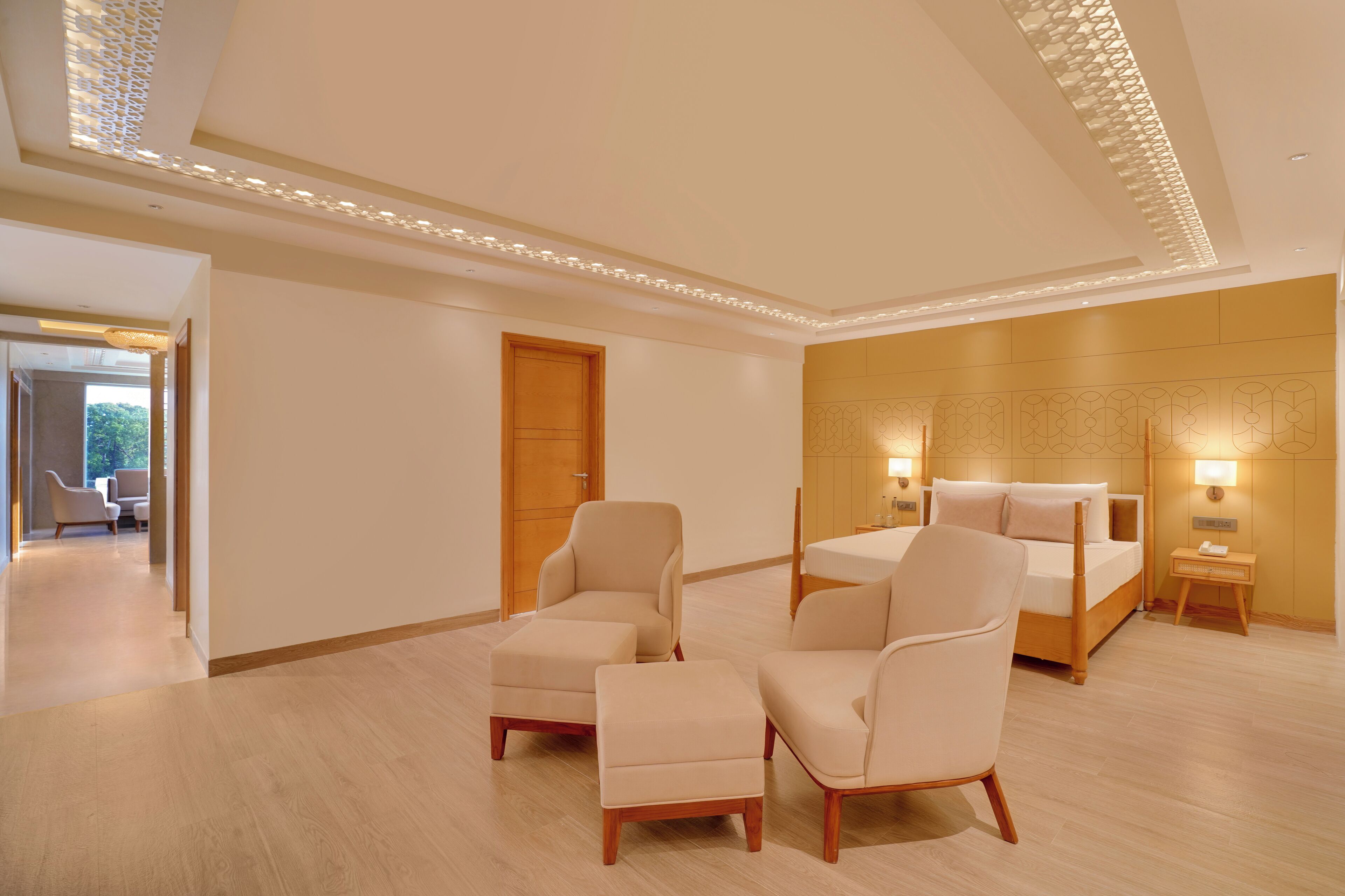 A modern hotel room with a wooden floor, a bed, two armchairs, a small table, and a nightstand with a lamp.