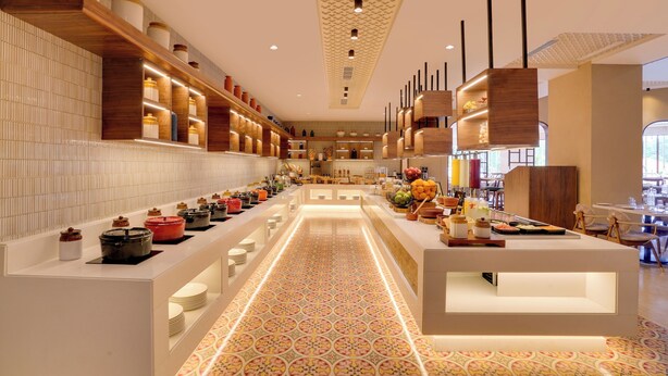 A modern hotel lobby with a long reception desk, wooden shelving with decorative items, patterned floor tiles, and a patterned ceiling. - Lemon Tree Premier Thiruvananthapuram (Thiruvananthapuram)