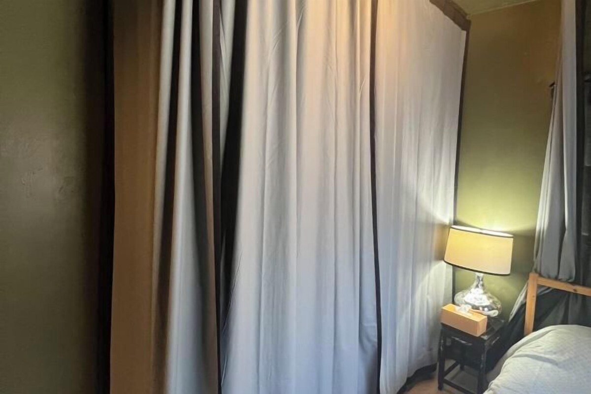 Una stanza con un letto, un comodino con una lampada e delle tende.
