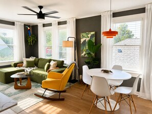 A modern living room with a green sofa, a yellow rocking chair, a white dining table, and a ceiling fan.