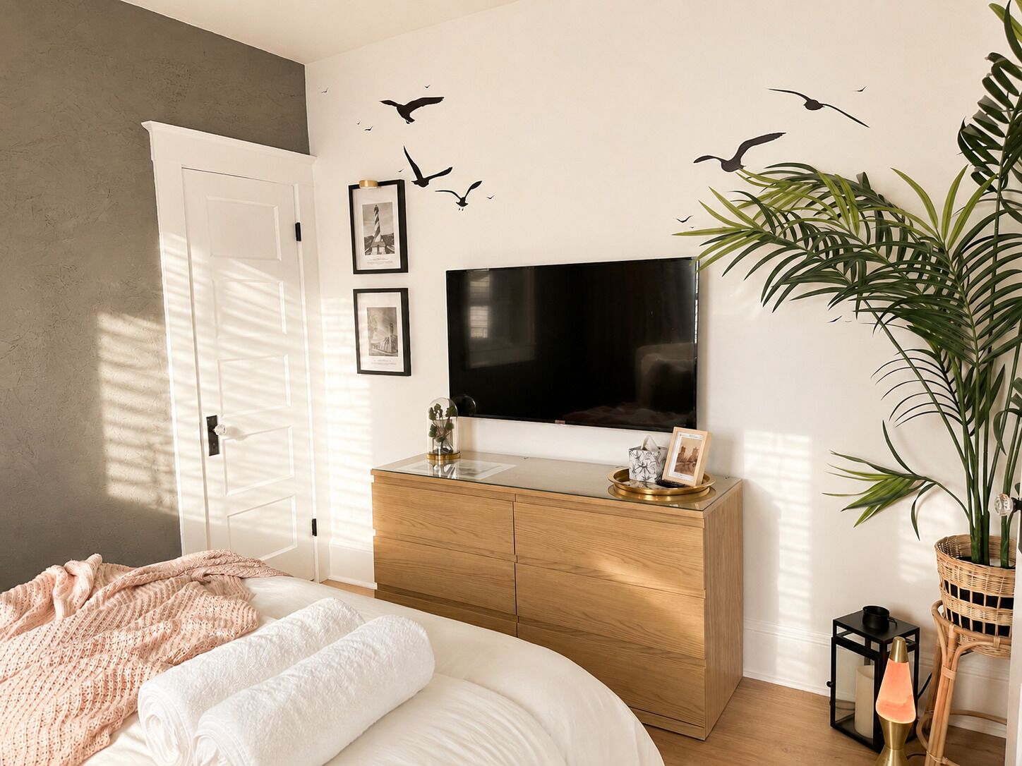 A bedroom with a bed, a dresser, a television, and a potted plant.