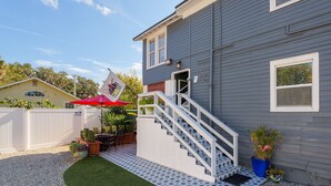 A two-story building with a staircase leading to the entrance, a small outdoor seating area with a red umbrella, and a flag with a heart symbol.