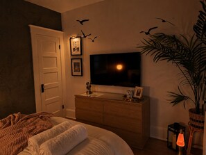 Un dormitorio con cama, cómoda, televisor, cuadros enmarcados y una planta.