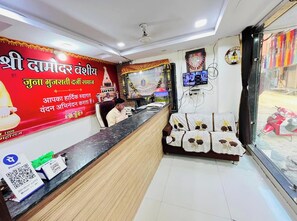 A reception area with a counter, a wall-mounted television, and a bed with a floral bedspread. - Satkar home stay ujjain (Ujjain)