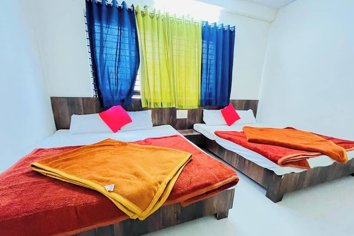 A hotel room with two beds, each with a red and yellow blanket, and a window with blue and yellow curtains.