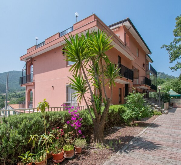 A pink two-story building with balconies, surrounded by greenery and potted plants. - Apartment  Turchese (Pietra Ligure)