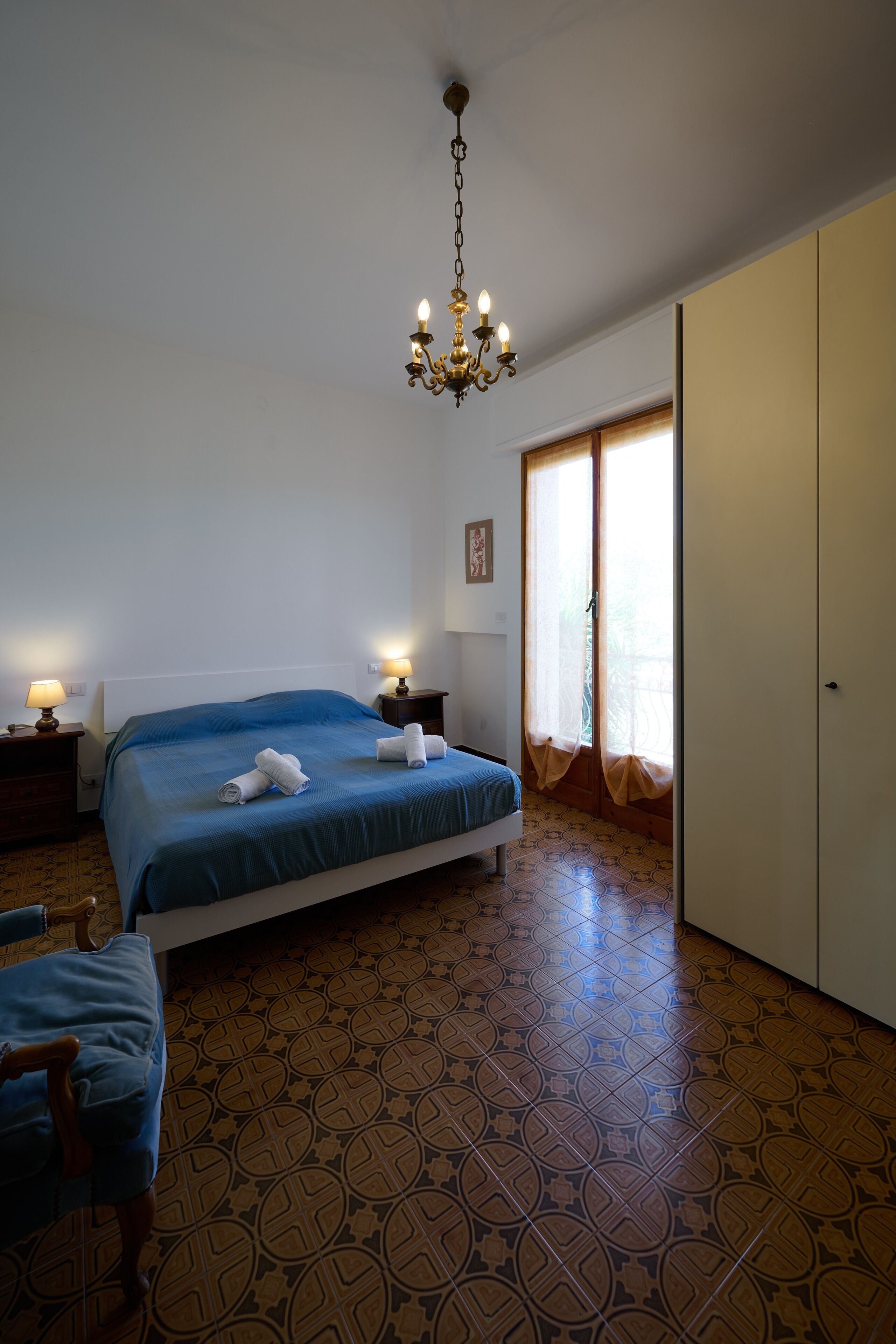Ein Schlafzimmer mit Bett, Nachttischen, einem Sessel, einem Kleiderschrank und einer Chandelier.