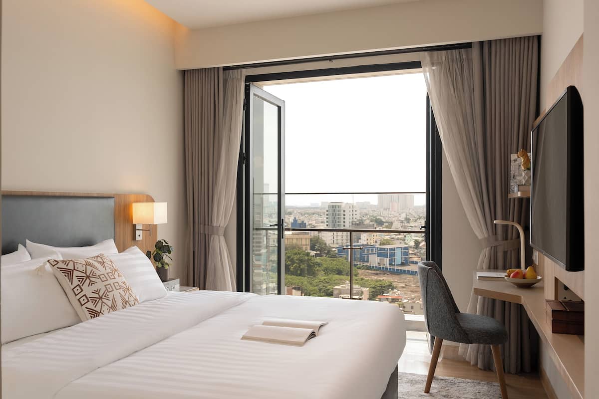 Une chambre d’hôtel avec un grand lit, un bureau avec une chaise, une télévision et une vue sur la ville grâce à une grande fenêtre.