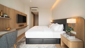 Una habitación de hotel moderna con una cama grande, un televisor de pantalla plana en la pared, un escritorio con una silla y una mesita de noche con una lámpara y una planta.