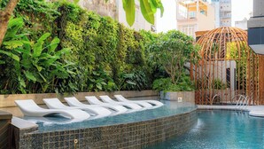 Una piscina de borde curvo, rodeada de abundante vegetación y una estructura de bambú.