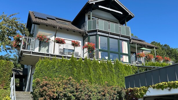A two-story building with balconies, large windows, and solar panels.