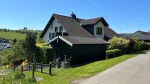A house with a sloped roof, a small attached shed, and a fenced yard with a pathway leading to the house.