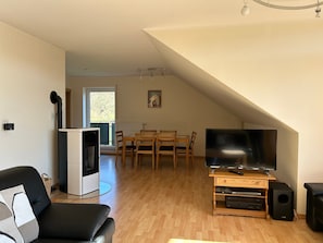 Una sala de estar con televisor, parlantes, un sofá y un comedor con sillas.