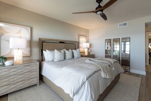 A bedroom with a bed, nightstands, a ceiling fan, and a large mirror.