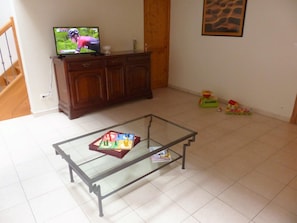 A living room with a glass-top coffee table, a television on a wooden cabinet, and children's toys on the floor.