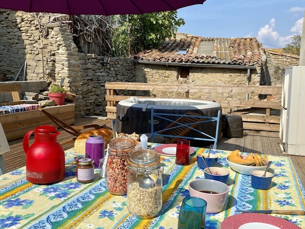 An outdoor dining area with a table set for a meal, surrounded by stone walls and a tiled roof.