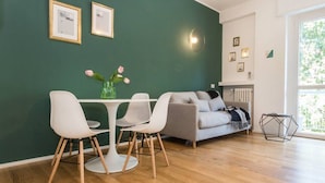 A modern living room with a dining area, featuring a green wall, a grey sofa, and a white table with chairs. - 2 Combined Flats Near CityLife District (Milan)