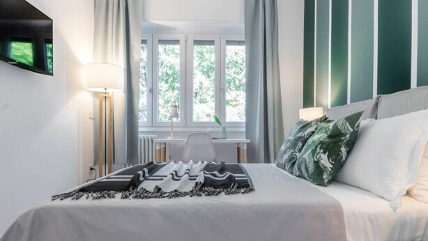 A neatly arranged bedroom with a bed, a desk, and a window with curtains. - 2 Combined Flats Near CityLife District (Milan)