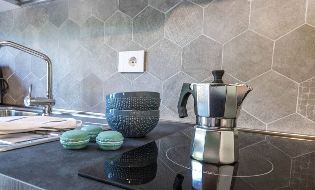 A kitchen with a modern design, featuring a stainless steel kettle, a black bowl, and a sink with a faucet.