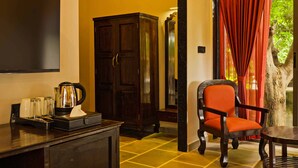 A hotel room with a wooden cabinet, a table with a chair, a television, and a window with red curtains. - Holiday Ranakpur (Desuri)