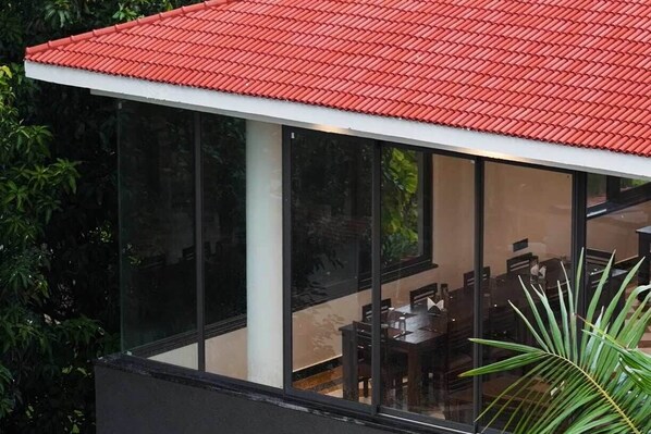 A modern building with a red-tiled roof, large glass windows, and a dining area with tables and chairs.