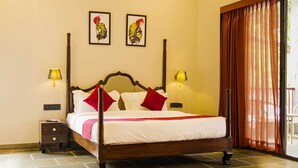 A four-poster bed with white linens and red pillows, a nightstand with a lamp, and two framed floral artworks on the wall. - Holiday Ranakpur (Desuri)