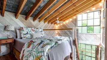 A bedroom with a wooden ceiling, a bed with patterned bedding, a nightstand, a lamp, and a window with a view.