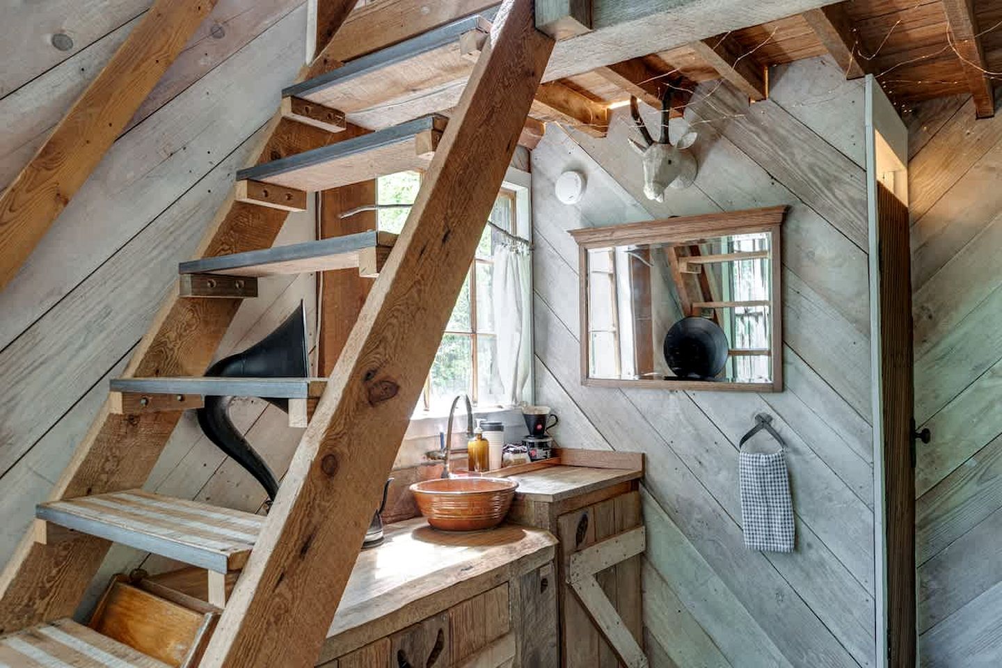 Ein rustikales Blockhaus-Interieur mit einer Holztreppe, einer Küchenzeile inklusive Spüle und einem Fenster mit Blick.