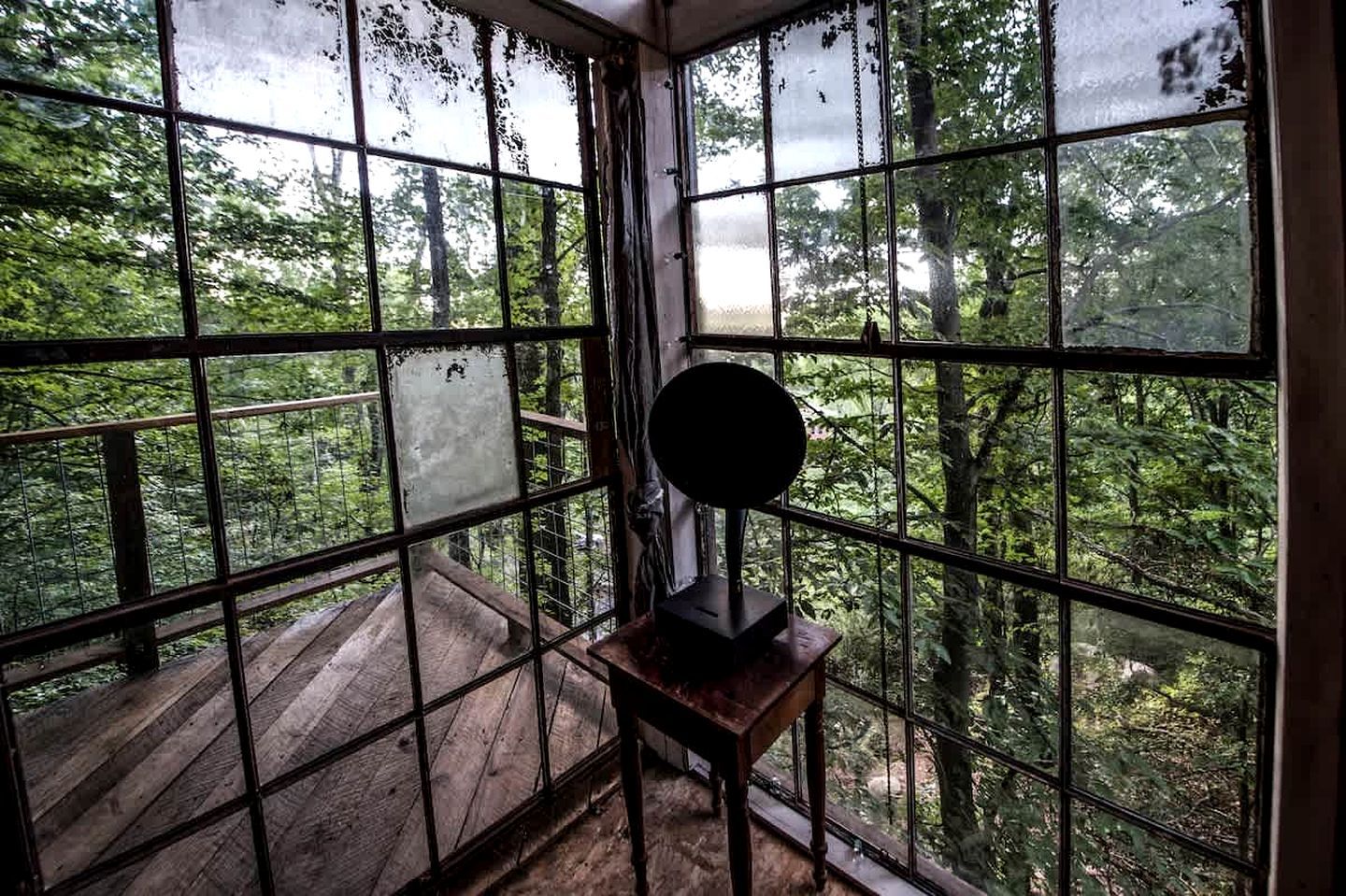 A room with large windows, a wooden deck outside, and a small table with a lamp.