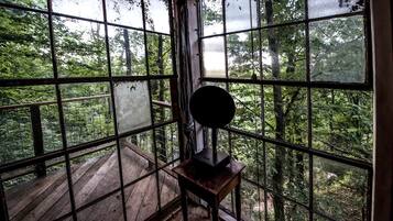 A room with large windows, a wooden deck outside, and a small table with a lamp.