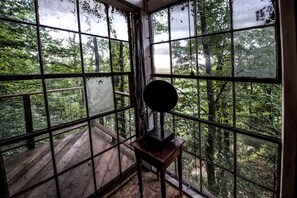 A room with large windows, a wooden deck outside, and a small table with a lamp.