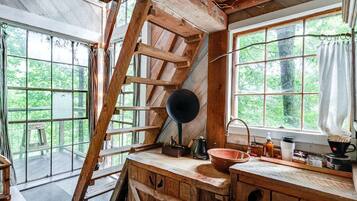 A rustic cabin interior with a wooden staircase, a large window, and a sink.