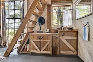 Una cabaña rústica con un dormitorio en el altillo, un escritorio de madera y una ventana con vistas a los árboles.