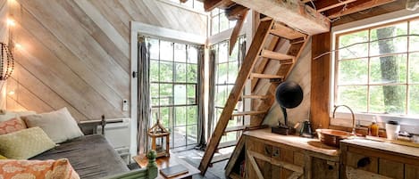 A rustic cabin interior with a loft bedroom, a wooden staircase, and a kitchen area.