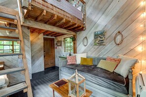 A loft-style bedroom with a loft bed, a wooden ladder, a small table, and a window with a view of greenery. - Secluded Tree House in the Forest near the Appalachian Mountains, Georgia (Flintstone)