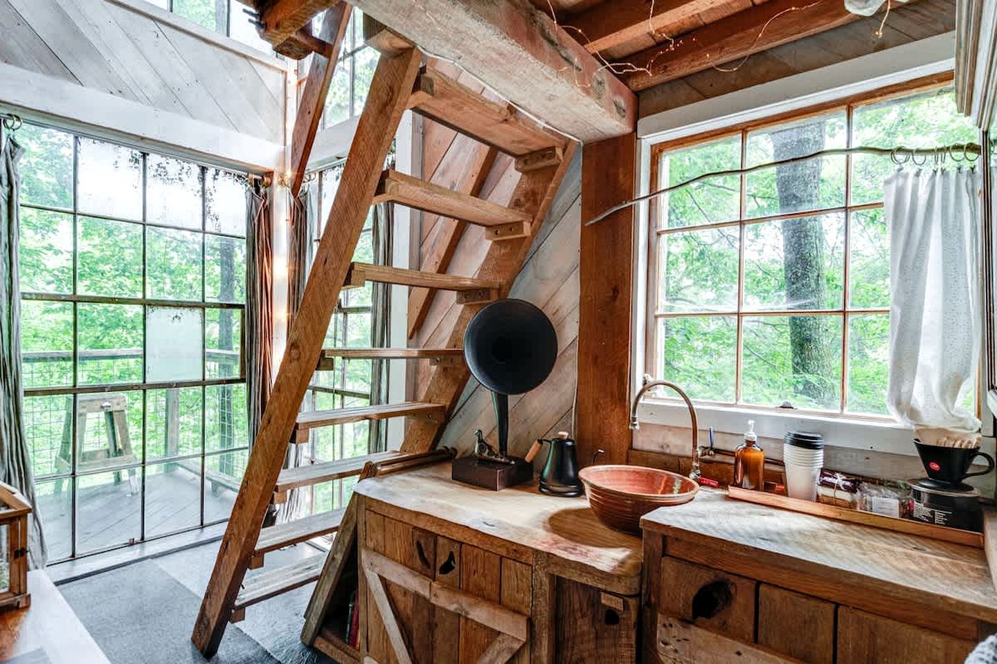 A rustic cabin interior with a wooden staircase, a large window, and a sink.
