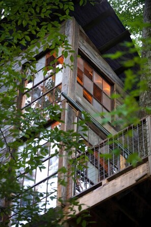 A multi-story building with large windows, a balcony, and a tree in the foreground.