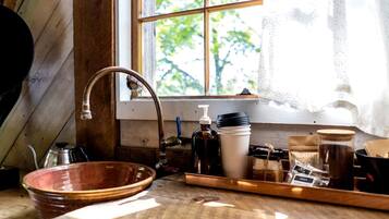 A rustic kitchen with a wooden sink, a window with a view of greenery, and various kitchen utensils and containers.