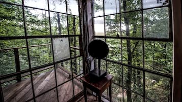 A room with large windows, a wooden deck outside, and a small table with a lamp.