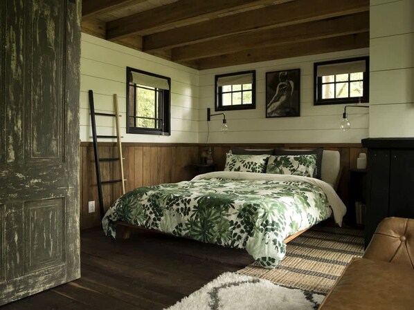 A bedroom with a bed, wooden walls, a ladder, and a door.